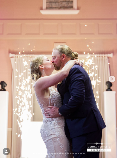 A couple in wedding attire kissing on a dance floor with bright indoor sparklers glowing behind them.